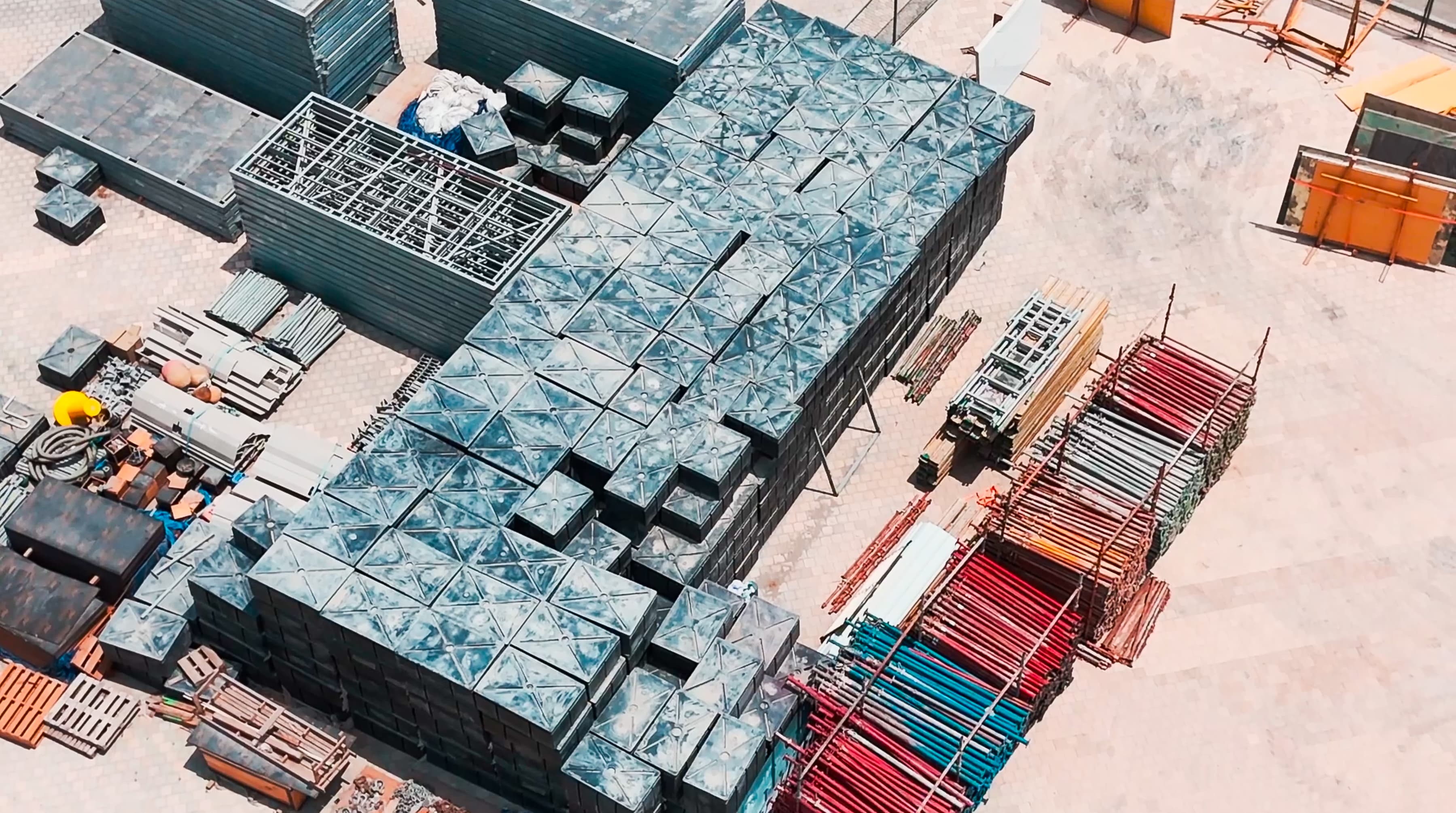 Aerial view of a construction site with neatly stacked metal scaffolding, colorful materials, and geometric patterns conveying order and industrial activity.